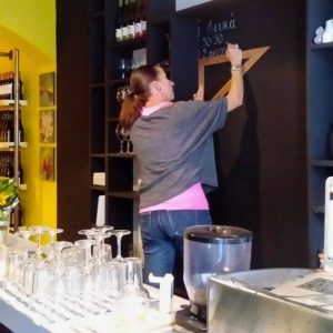 Team member preparing the chalkboard wine list at Cinque Wine & Deli, showcasing wines by the glass during the early days of the wine bar in Athens.
