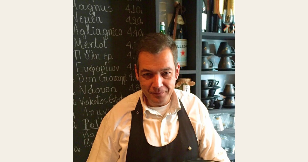 Cinque Wine & Deli team member in front of Greek wine list chalkboard inside wine bar in Psyrri Athens.