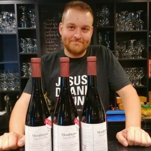 Nikitas Prassas holding Cinque Wine & Deli labeled bottles created for the “A Wine for a Scholarship” initiative supporting the American Farm School of Thessaloniki.