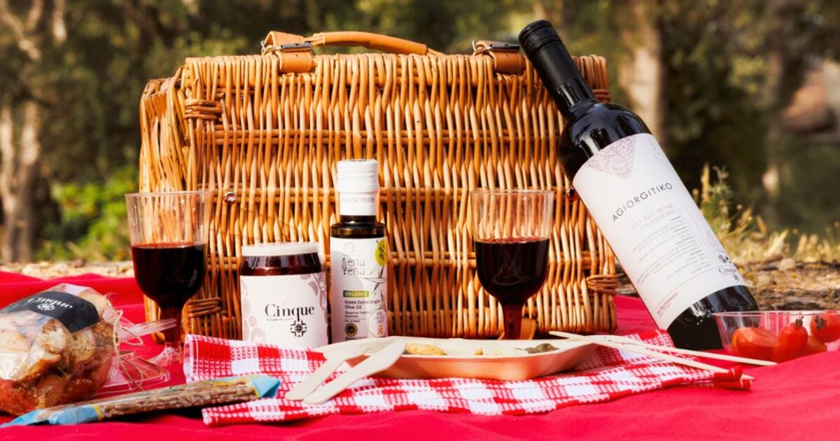 Cinque Picnic Box with bottle of Greek Agiorgitiko wine, chutney, olive oil and picnic basket set on red blanket outdoors in Athens.