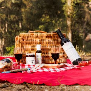 Cinque Picnic Box with bottle of Greek Agiorgitiko wine, chutney, olive oil and picnic basket set on red blanket outdoors in Athens.