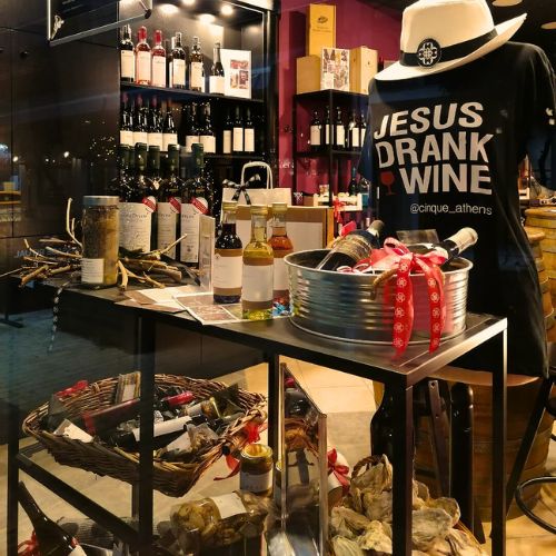 Cinque Go retail display featuring Greek wines, gift boxes, and branded products for takeaway. Greek wine, gifts, and deli — ready to go.