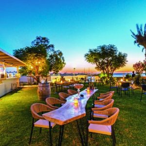 Outdoor garden setting at Cinque Mykonos during sunset, featuring tables set for wine and social gatherings in a seasonal Mediterranean atmosphere.