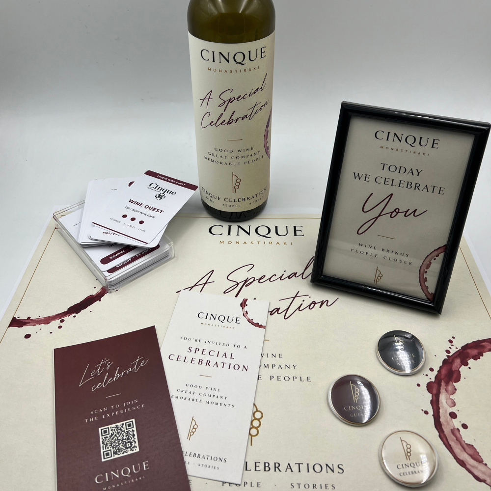 Cinque Celebrations setup with Greek wine, personalised celebration bottle, Wine Quest cards, pins and keepsake frame at Cinque Monastiraki