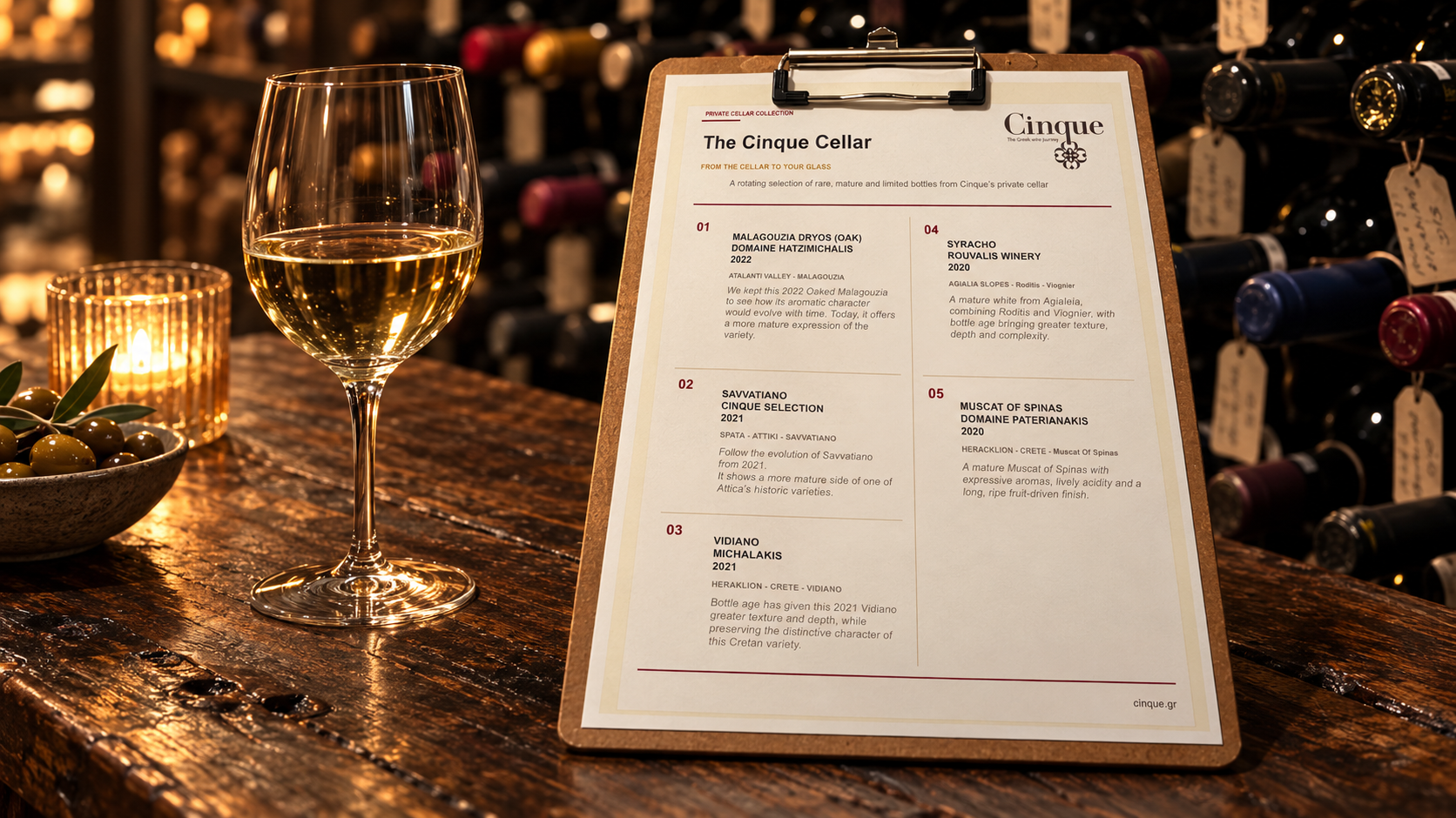 The Cinque Cellar wine list on a wooden table beside a glass of wine, in an illustrative cellar setting.