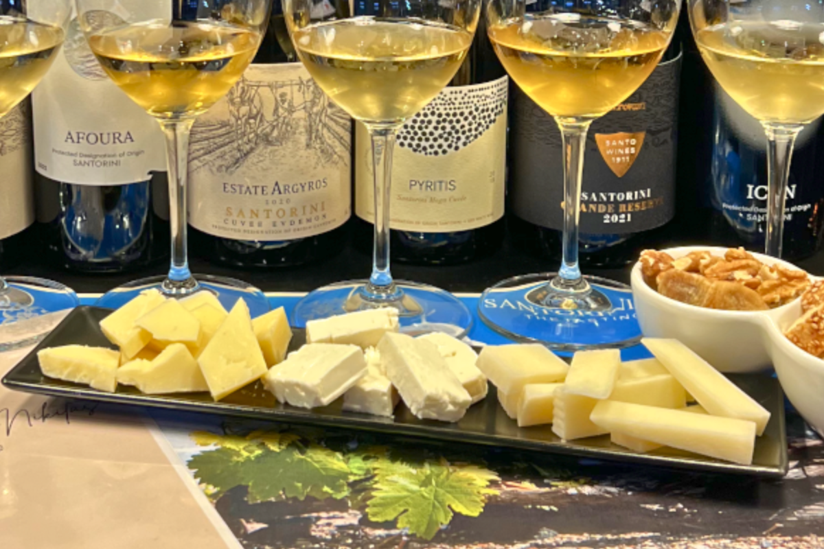 Small groups of cheese pieces on a black tasting plate beside wine glasses