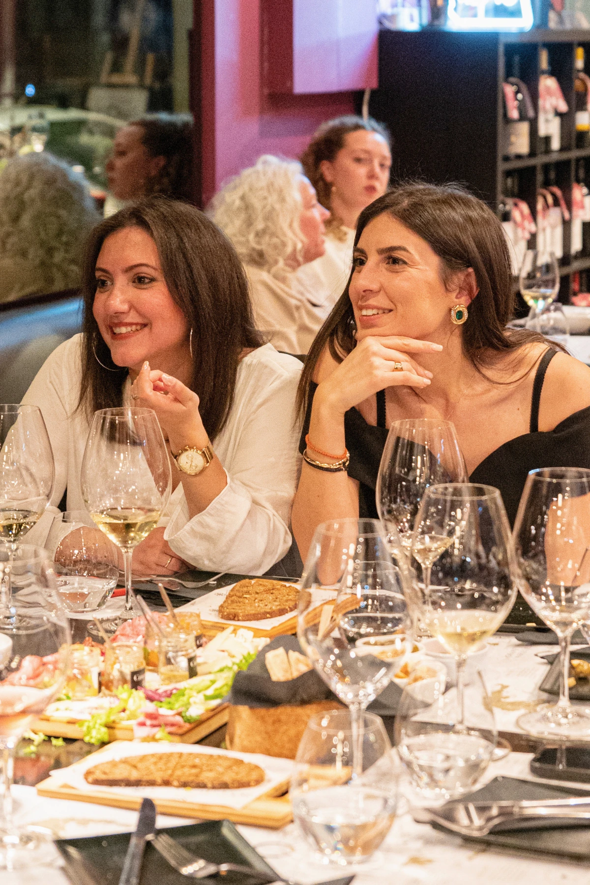 Two guests smiling at a table with wine glasses and food at Cinque in Athens.